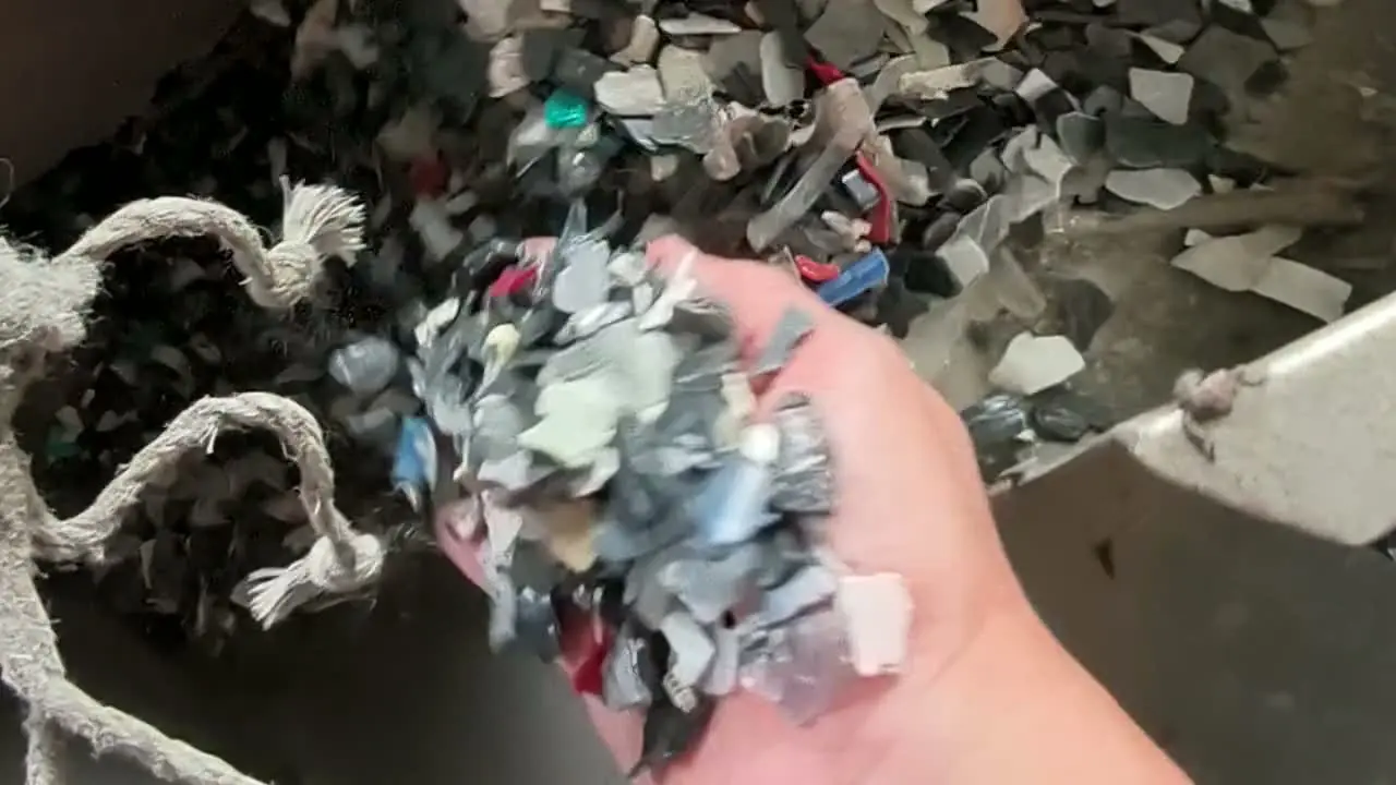 A hand lifting crushed plastic flakes out of the feed