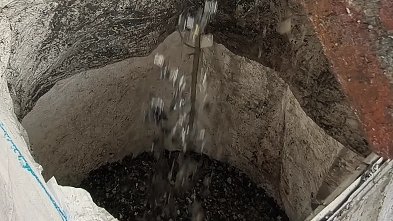 Plastic flakes fall from a crusher chute into a white bulk bag