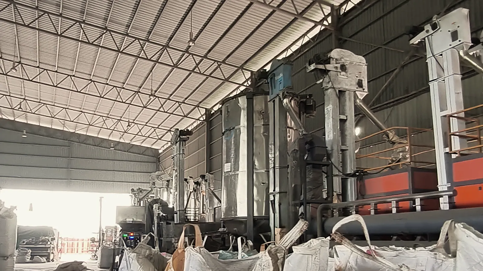 A processing line inside a shed, with filled bulk bags standing in front of it
