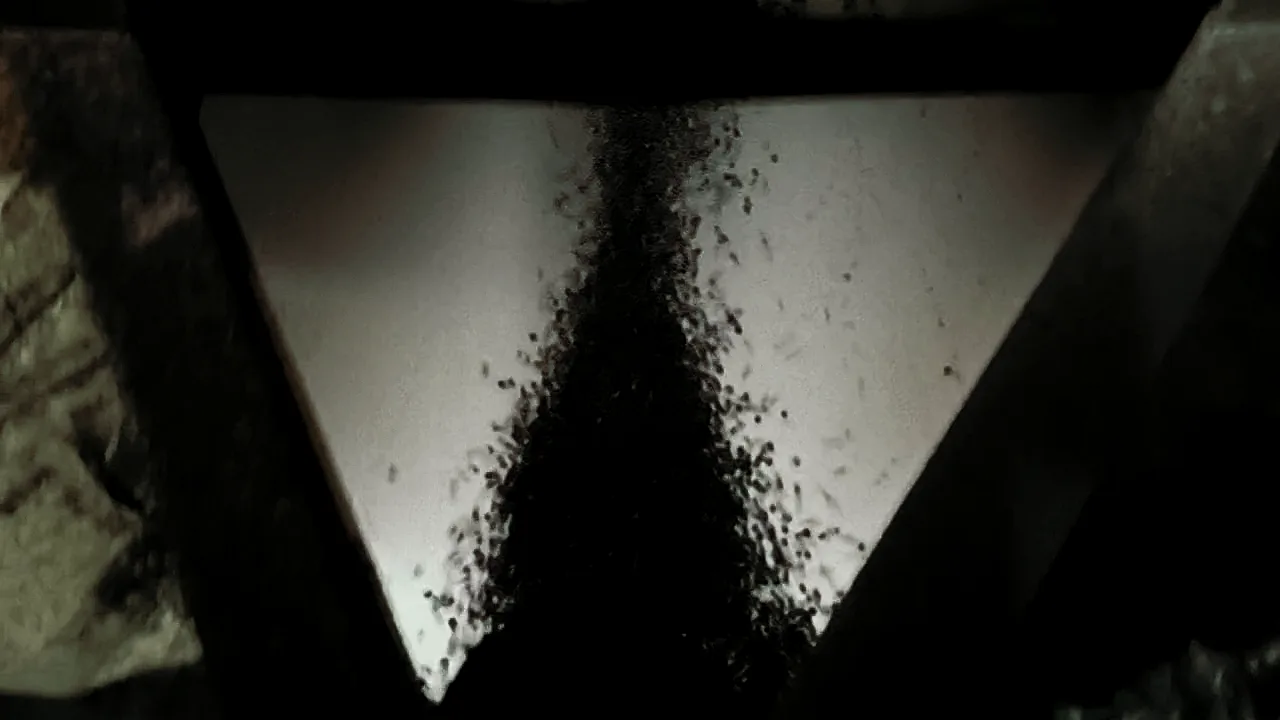Dark recycled pellets pouring down through a steel hopper