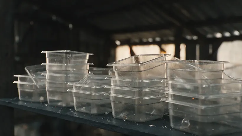 Stacks of clear rigid plastic containers and lids on a dark shelf (illustration)