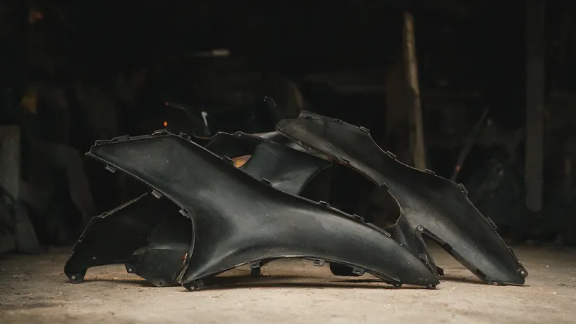 Unpainted black moulded motorbike fairing panels leaning against a workshop wall (illustration)